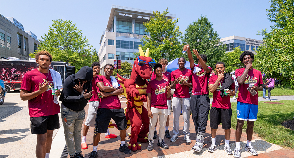 Howard Community College students and the college’s dragon mascot pose together outdoors during Summer Bash, wearing HCC Dragons T-shirts.