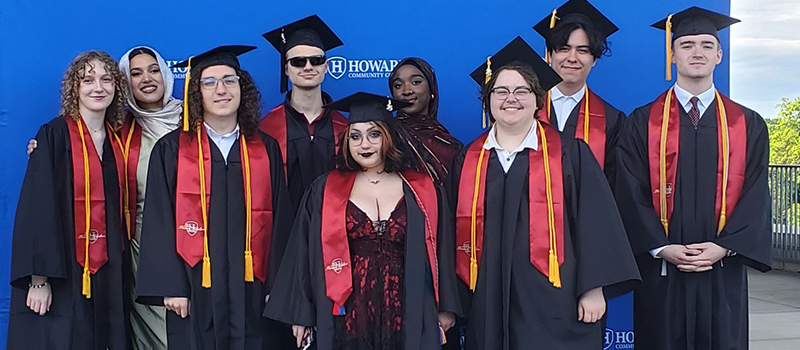 Eight HCC students in caps and gowns pose together at commencement.