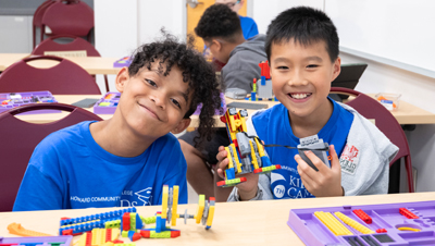 Two Kids on Campus students smile while showing off their colorful building projects made with construction bricks in a classroom at Howard Community College.